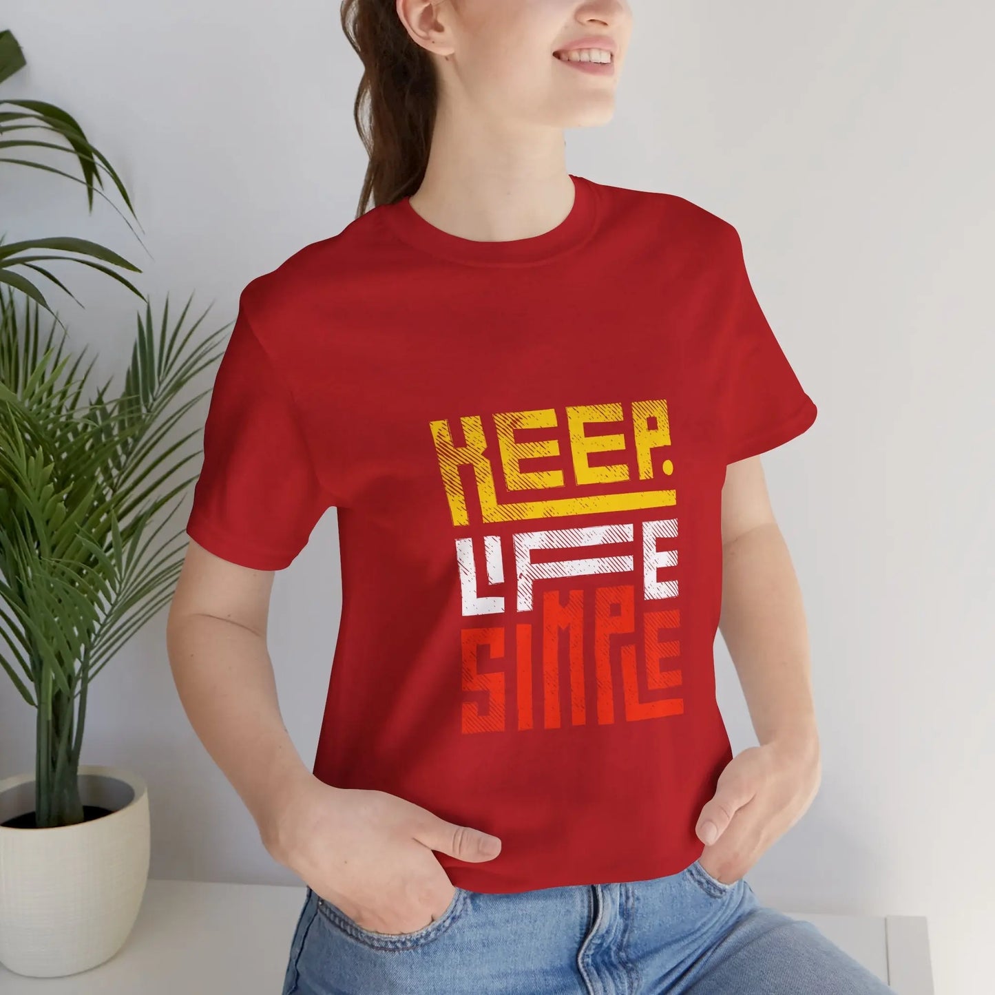Frau mit einem roten T-Shirt mit dem Motiv "Keep Life Simple", sitzt entspannt in einem modernen Innenraum.