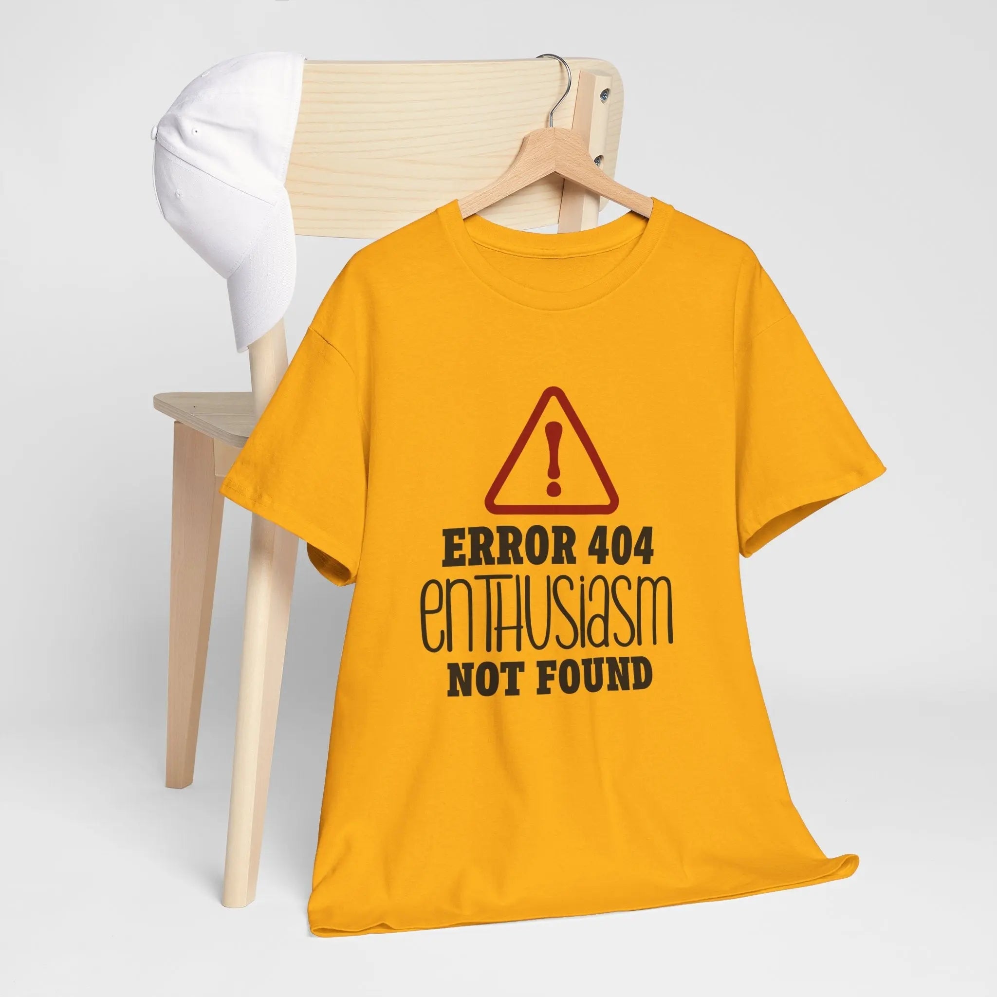 Gelbes T-Shirt mit „Error 404 Enthusiasm Not Found“-Print hängt über einem Holzstuhl, daneben eine weiße Baseballmütze.