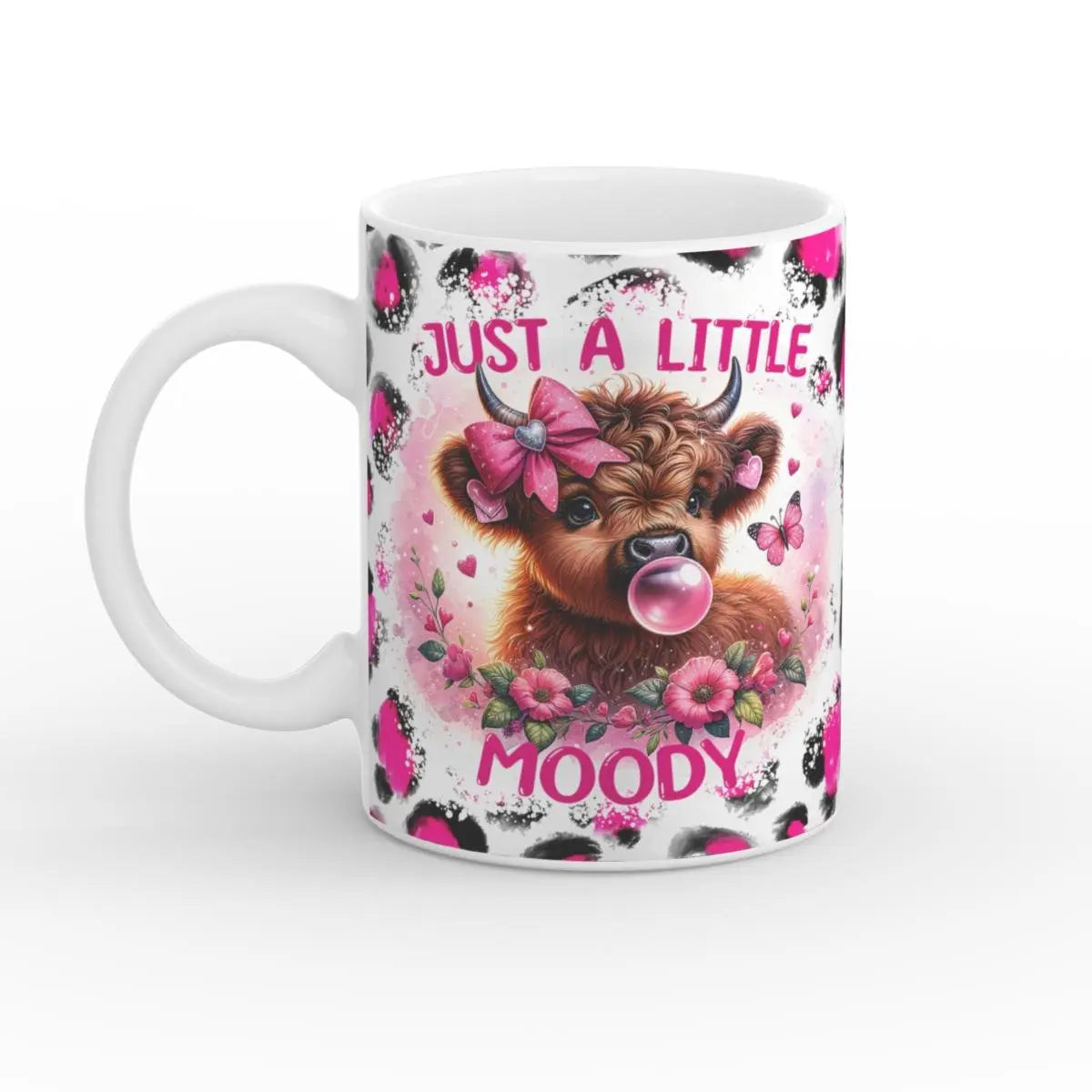 Weiße Keramiktasse mit einem verspielten Design: eine süße Highland-Kuh mit rosa Schleife und einer Kaugummiblase, umgeben von rosa Blumen, Schmetterlingen und schwarzen, gepunkteten Akzenten. Der Text „Just a Little Moody“ steht prominent über und unter der Kuh.