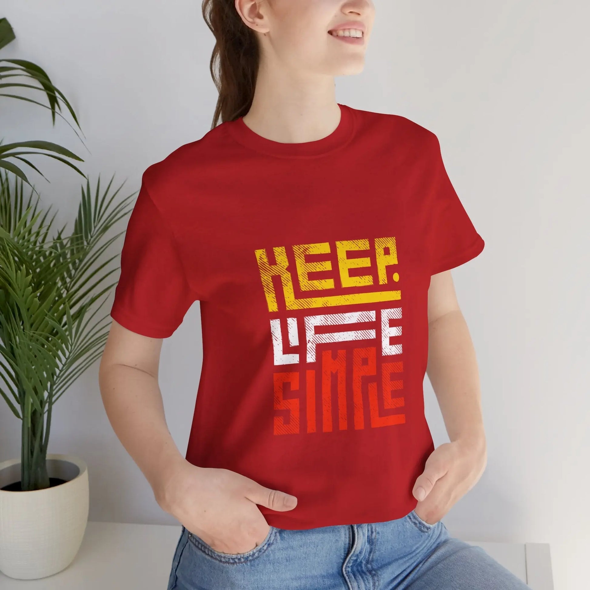 Frau mit einem roten T-Shirt mit dem Motiv "Keep Life Simple", sitzt entspannt in einem modernen Innenraum.